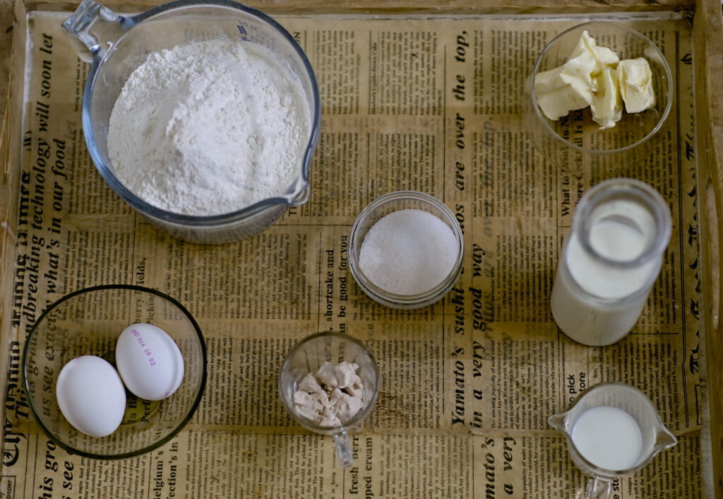 Auf einem Tablett stehen folgende Zutaten: Mehl, Butter, Zucker, Hefe, Eier , Milch 