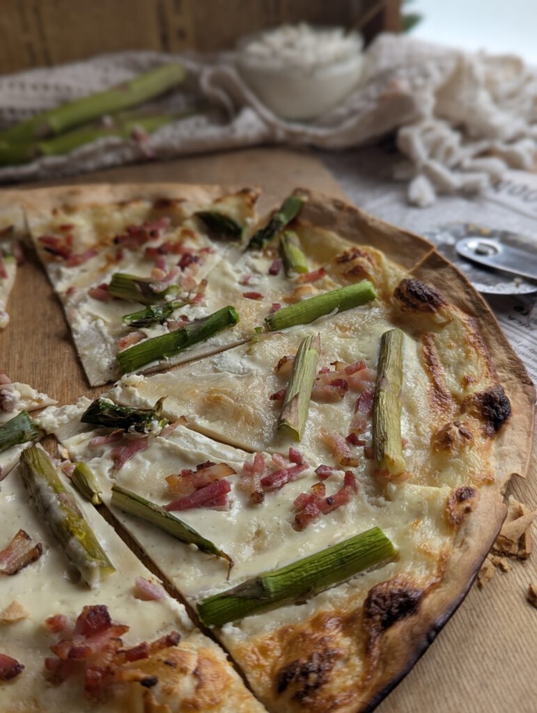 auf einem Holzbrett liegt ein Flammkuchen mit Spargel