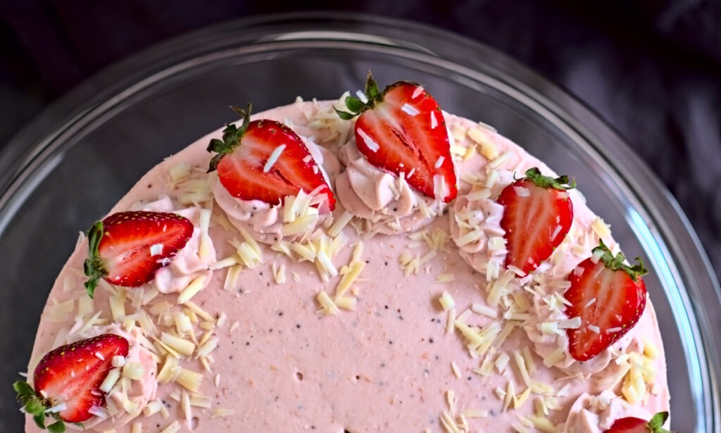 Cremige Erdbeer-Sahne-Torte als Nahaufnahme zeigt die Dekoration auf der Oberfläche. In aufgespritzte Sahnetupfen wurden halbierte Erdbeeren gedrückt und mit weißen Schokoladenraspeln verziert.
