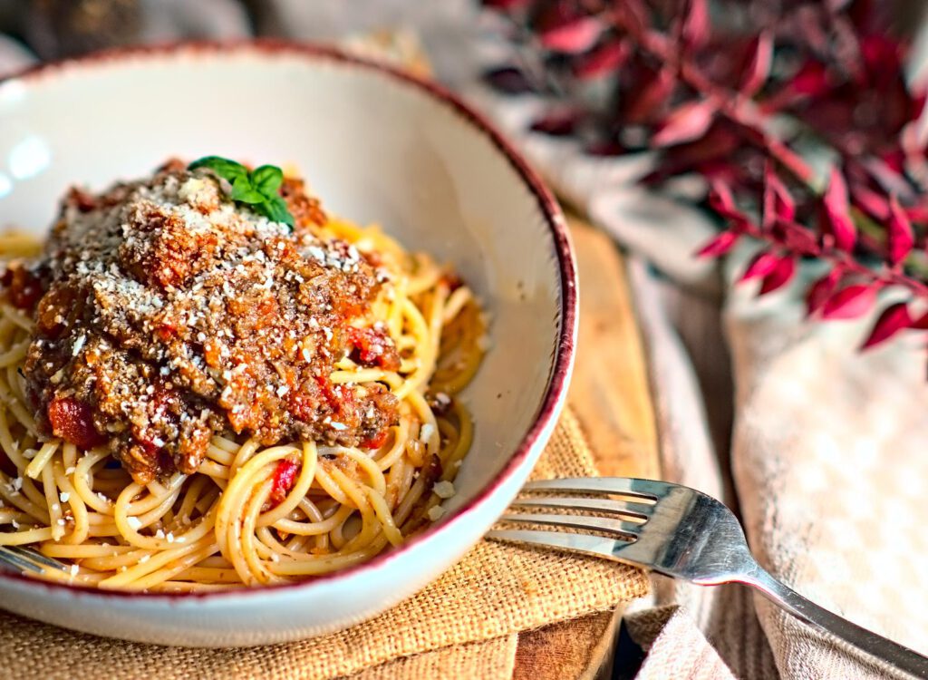 Veggie Bolognese aus Pilzen auf Spaghetti mit Hartkäse in einem tiefen Teller auf einem Holzbrett