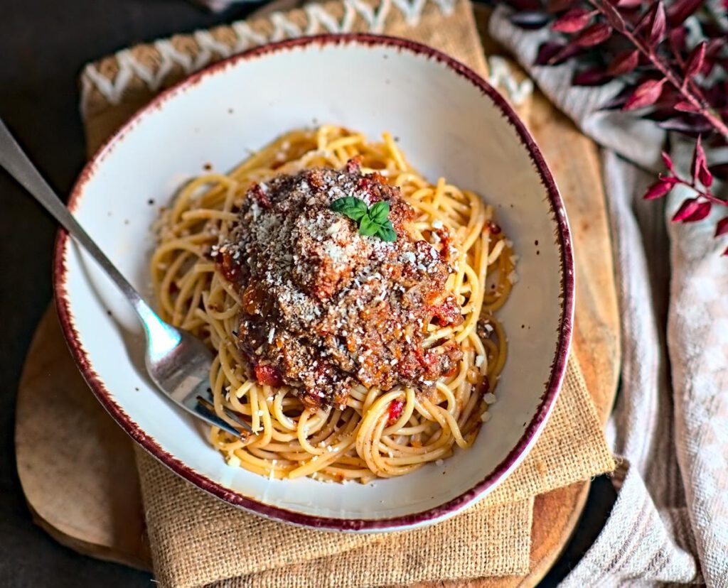 Spaghetti getoppt mit Veggie Bolognese aus Pilzen und serviert mit geriebenem Hartkäse und Basilikum