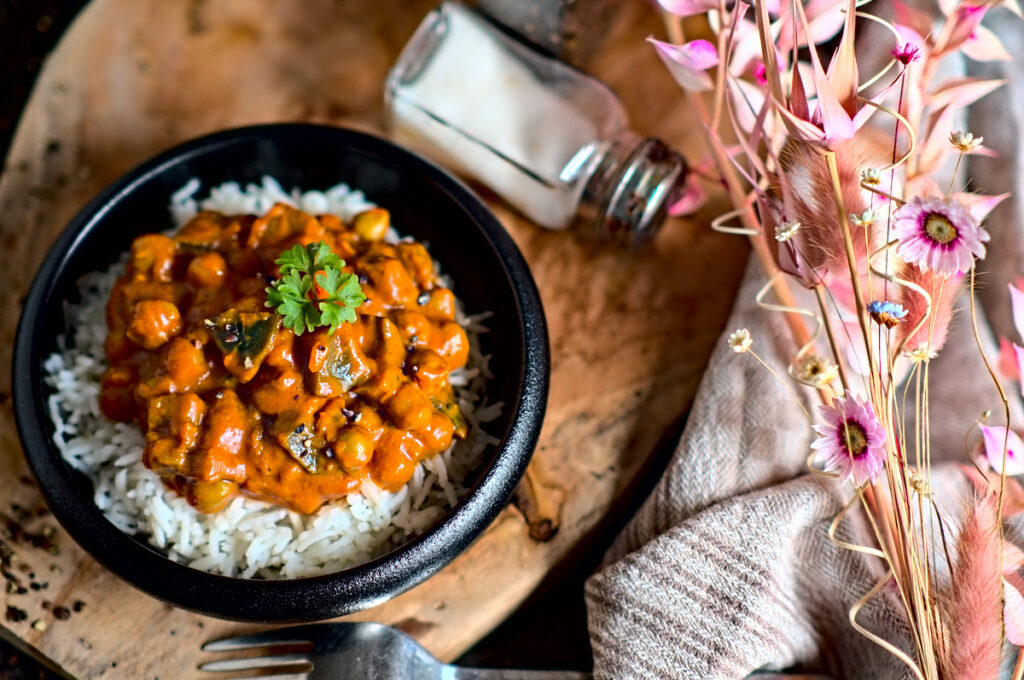 farbenfrohes Kichererbsen Curry mit Aubergine auf Reis in einer schwarzen kleinen Schüssel