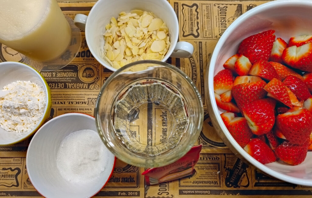 Zutaten für den Belag des Erdbeerkuchens: Vanillepuddingpulver, Zucker, Milch, Erdbeeren, Tortenguss, Wasser und Mandelblätter als Deko