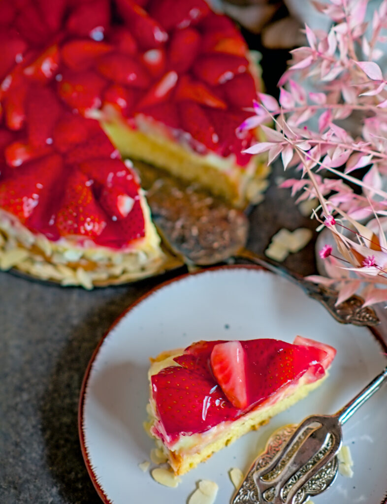 ein Stück Erdbeerkuchen mit Vanillepudding angeschnitten auf dem Teller