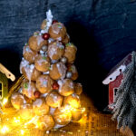 auf dem Bild sieht man einen Windbeutel-Weihnachtsbaum mit kleinen Tannen, Häuschen und Lichterkette