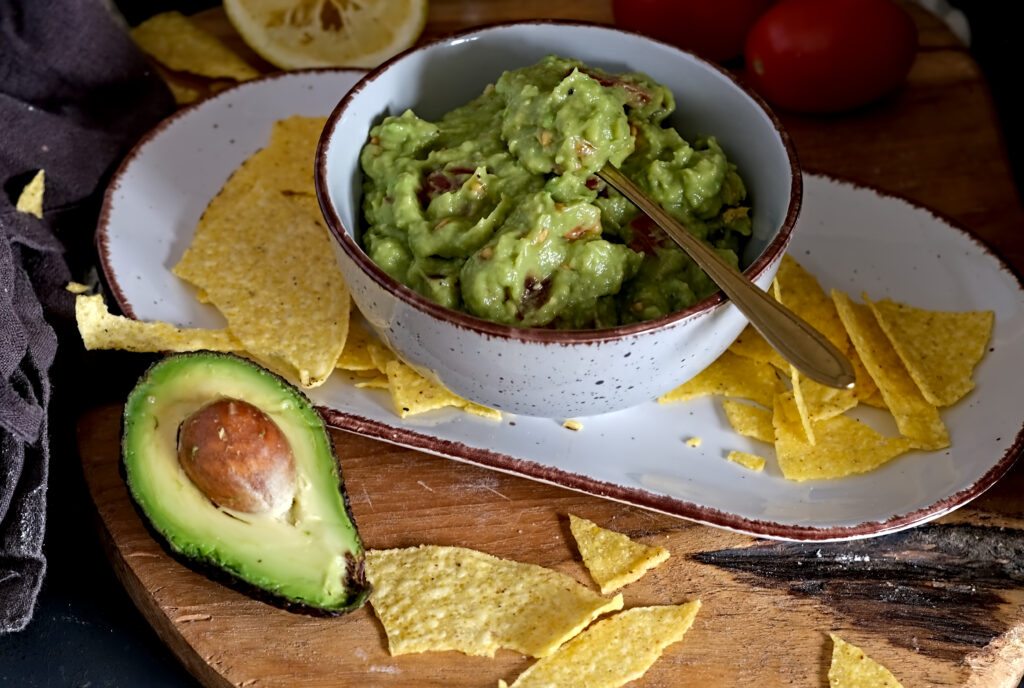 auf dem Bild sieht man eine Schüssel mit Guacamole, daneben liegt eine aufgeschnittene Avocado