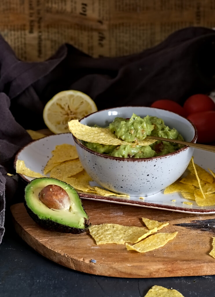 auf dem Bild sieht man eine Schüssel mit Guacamole, davor liegt eine Avocado mit Kern