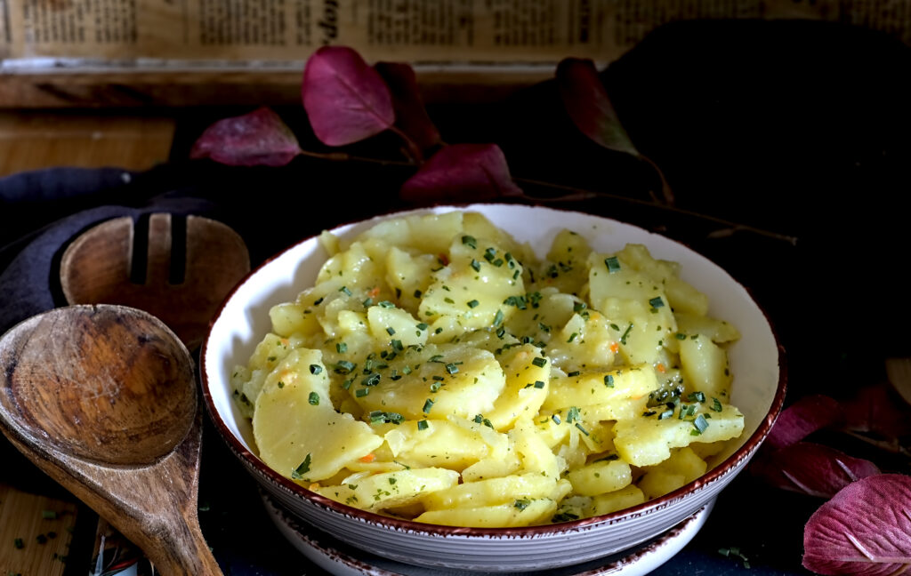 auf dem Bild siehst du eine Schüssel in der sich badischer Kartoffelsalat befindet mit Holzlöffeln daneben