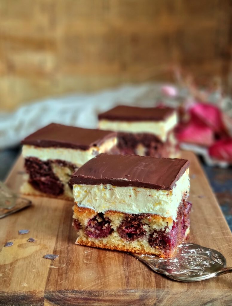 Ein saftiges Stück Donauwelle, man sieht deutlich die Schichten aus hellem und dunklem Teig, Kirschen, Buttercreme und dem typischen gewellten Schokoguss.