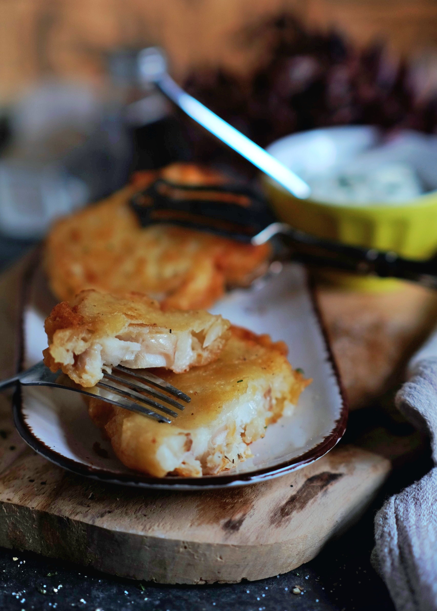 Nahaufnahme von einem knusprigen Backfisch, der aufgeschnitten ist und das saftige, weiße Fischfilet im Inneren zeigt
