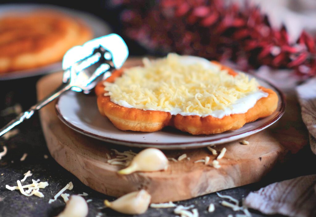 Goldbraun ausgebackener Langos mit Sauerrahm, Käse und Knoblauchöl auf einem rustikalen Teller serviert