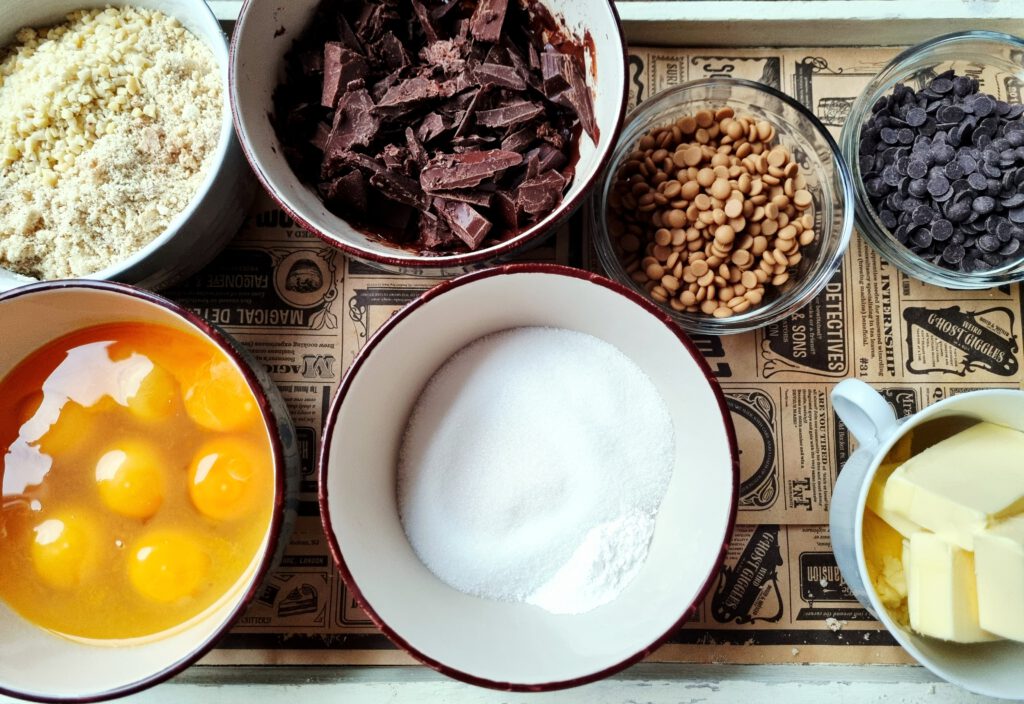 Zutaten für Brownies: gemahlene Nüsse, Eier, Zucker, Schokolade, Schokoladentropfen, Butter