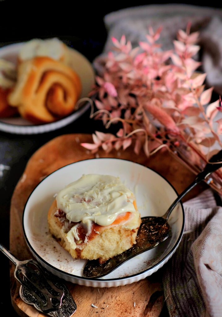 Fluffige Zimtschnecken mit weißem Frischkäse-Frosting auf einem Kuchenteller serviert