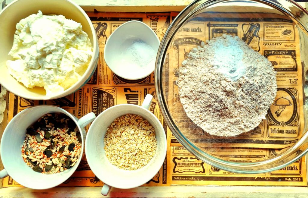 Zutaten für einfache Proteinbrötchen: Magerquark, Mehl, Backpulver, Salz, Haferflocken und optional Saaten stehen auf der Arbeitsfläche bereit