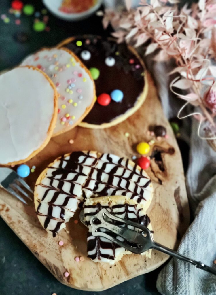 Stapel von frisch gebackenen Amerikanern auf einem rustikalen Holzteller mit verschiedener Deko: Schokogesicht mit Schokolinsen, Zuckerguss und bunten Streuseln und im schwarz-weiß Look