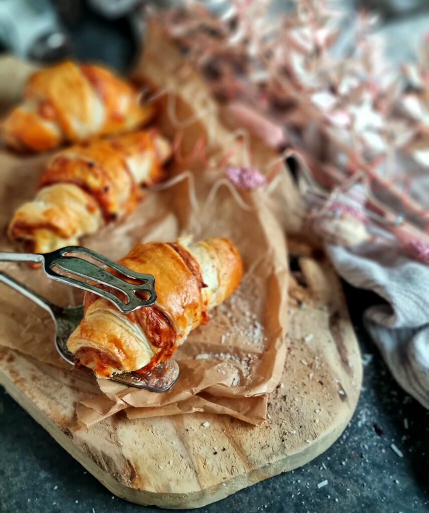 Ein goldbraun gebackenes Käse-Schinken-Croissant auf einem Holzbrett