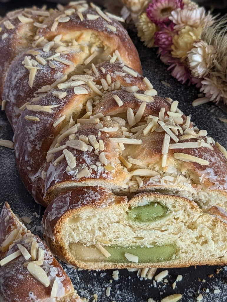 Nahaufnahme des Marzipan Zopf der auf einer schwarzen Unterlage liegt. im Hintergrund befinden sich trockenblumen
