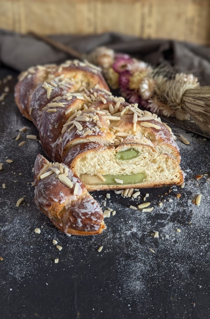 Marzipan Zopf der auf einer schwarzen Unterlage liegt. im Hintergrund befinden sich trockenblumen