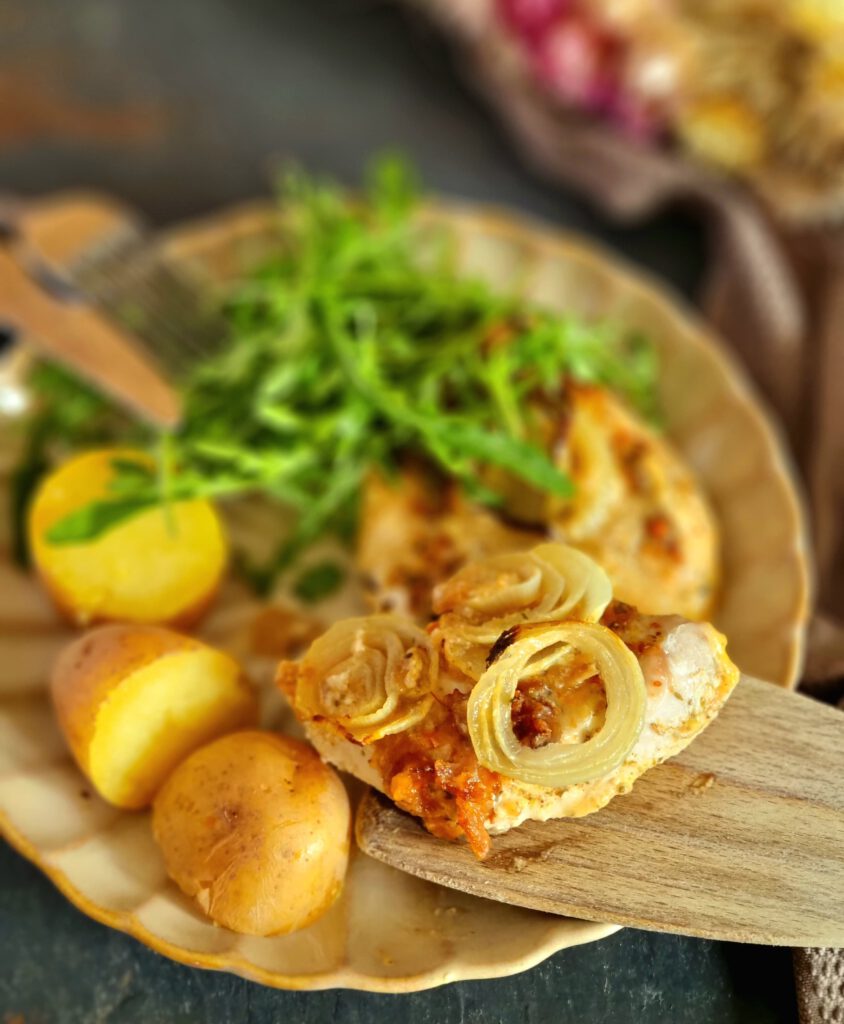 auf einem Teller befindet sich ein Zwiebel-Hähnchen mit Kartoffelhälften und Salat