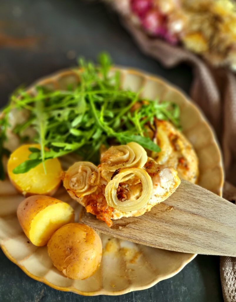 Zwiebel-Sahne-Hähnchen welches gerade auf einen Teller gelegt wird
