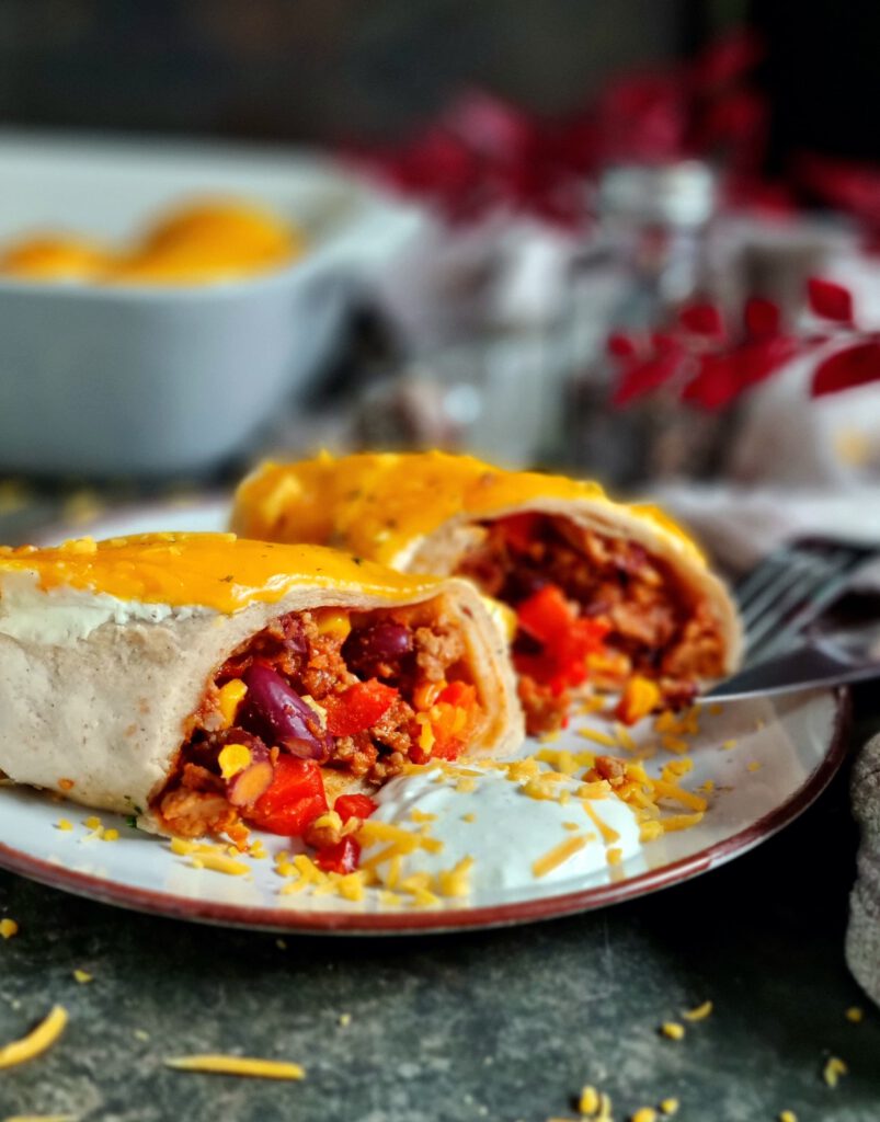 Herzhafter Hackfleisch-Enchilada mit geschmolzenem Käse und Schmand auf einem grauen Teller und rustikaler Schieferplatte