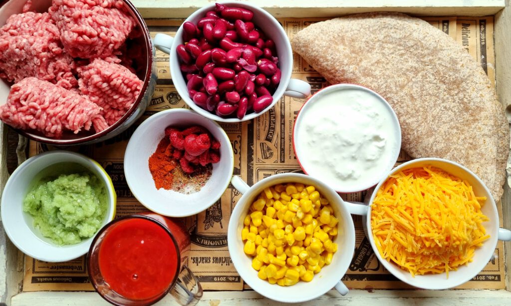 Zutaten für die Enchiladas: Zwiebel-Knoblauchpaste, Tomatenmark, Hackfleisch, passierte Tomaten, Gewürze, Kidneybohnen, Mais, Schmand, Wraps, Cheddar