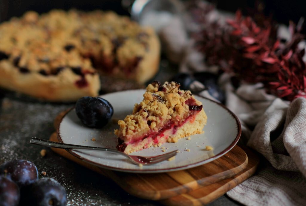 angeschnittenes Stück Zwetschgenkuchen, die die Schichten von Quark-Öl-Teig, saftigen Früchten und knusprigen Streuseln zeigt